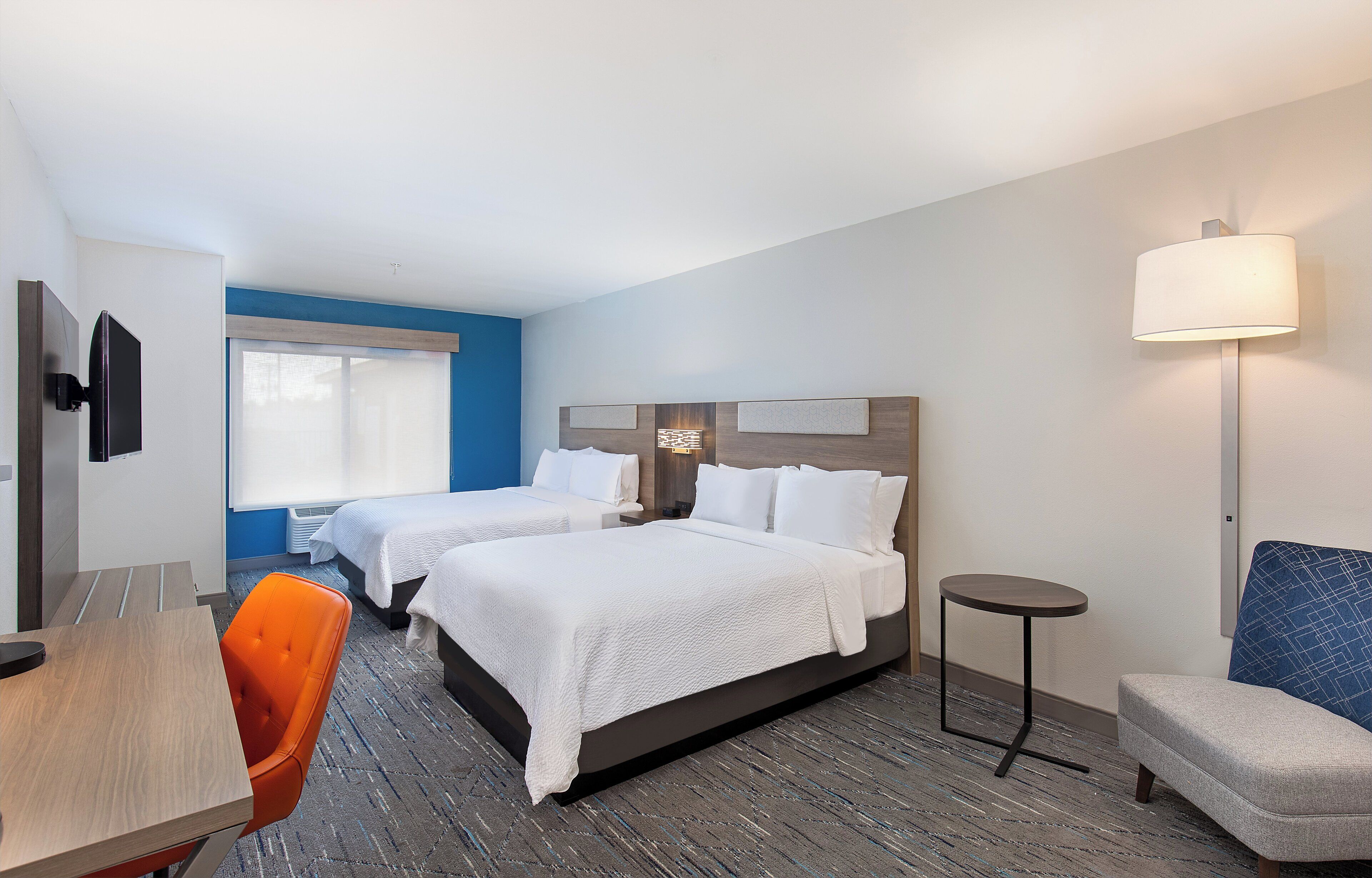 Une chambre d’hôtel avec deux lits, un bureau, une chaise et une lampe.