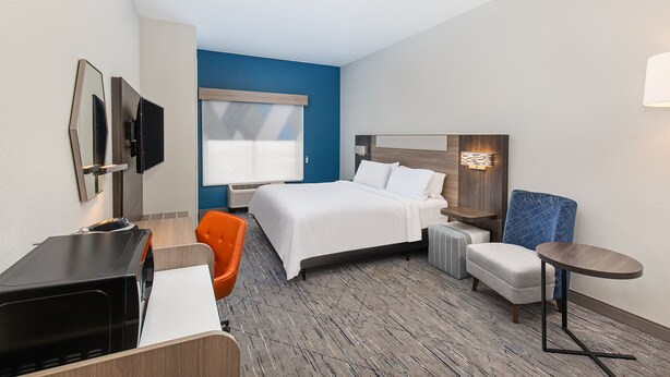 Ein Hotelzimmer mit Bett, Schreibtisch, einem orangefarbenen Sessel, einem kleinen Tisch und einem an der Wand befestigten Fernseher.