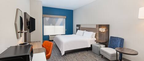 A hotel room with a bed, a desk, an orange chair, a small table, and a wall-mounted TV.