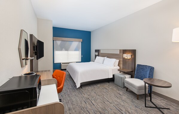 Ein Hotelzimmer mit Bett, Schreibtisch, einem orangefarbenen Sessel, einem kleinen Tisch und einem an der Wand befestigten Fernseher.