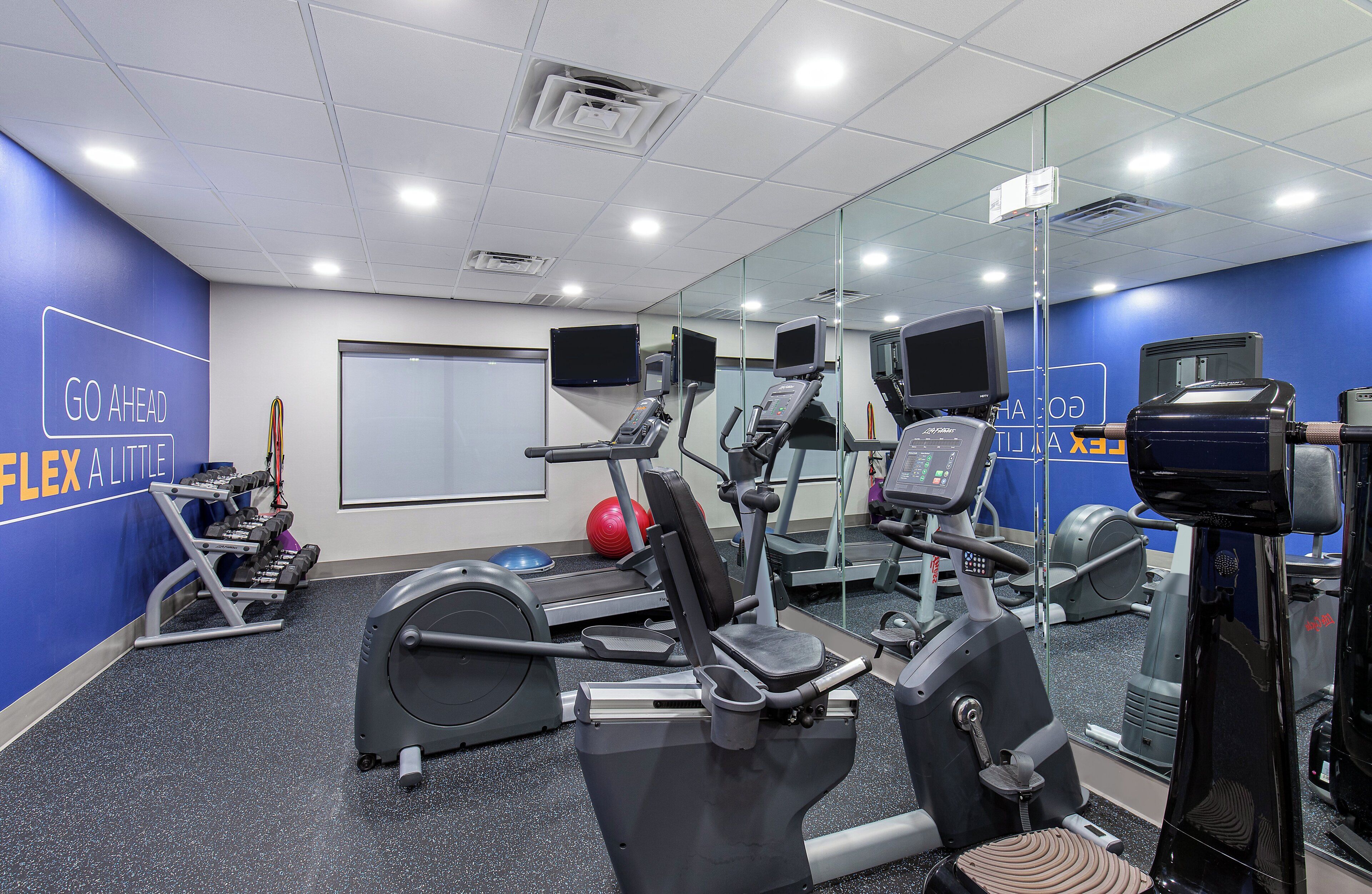 A gym with cardio machines, weights, and a mirrored wall.