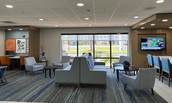 A hotel lobby with seating, a TV displaying weather, and large windows offering a view of the street. - Holiday Inn Express Savannah South I-95 - Richmond by IHG (Richmond Hill)