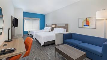 Quarto de hotel com duas camas, uma escrivaninha, uma cadeira, um sofá e uma televisão.