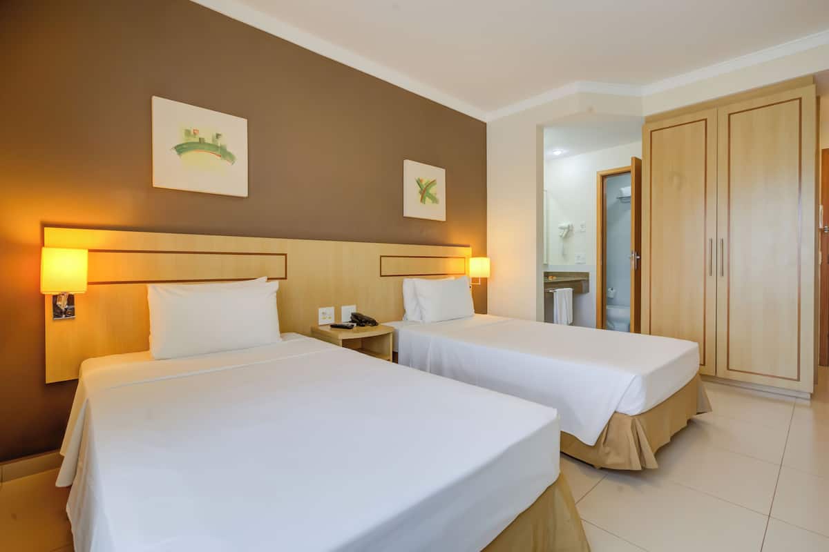 Habitación de hotel con dos camas, un armario de madera y un baño visible a través de una puerta abierta.