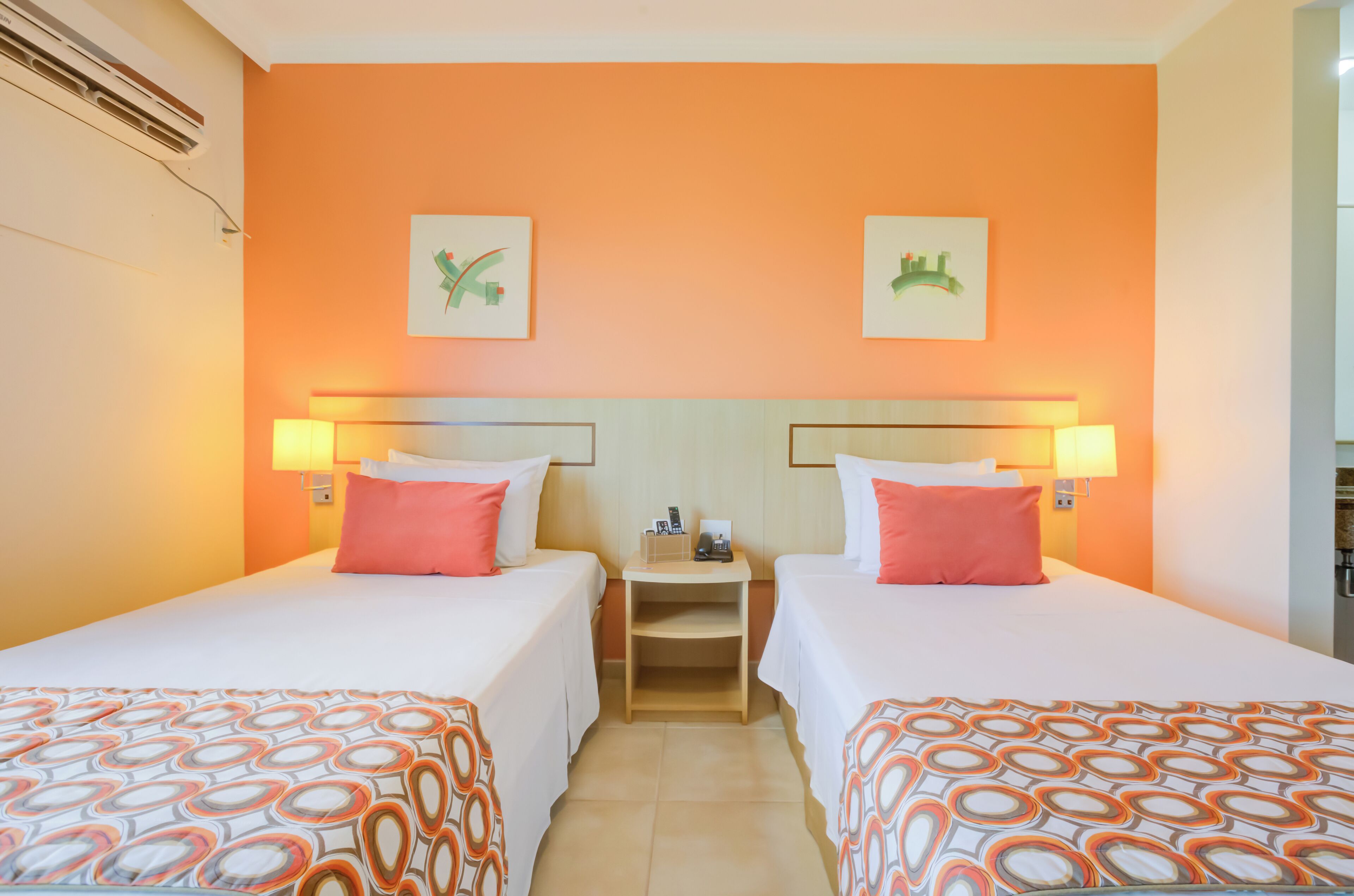 A hotel room with two beds, orange walls, and artwork above the beds.