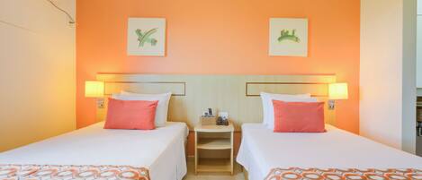 A hotel room with two beds, orange walls, and artwork above the beds.