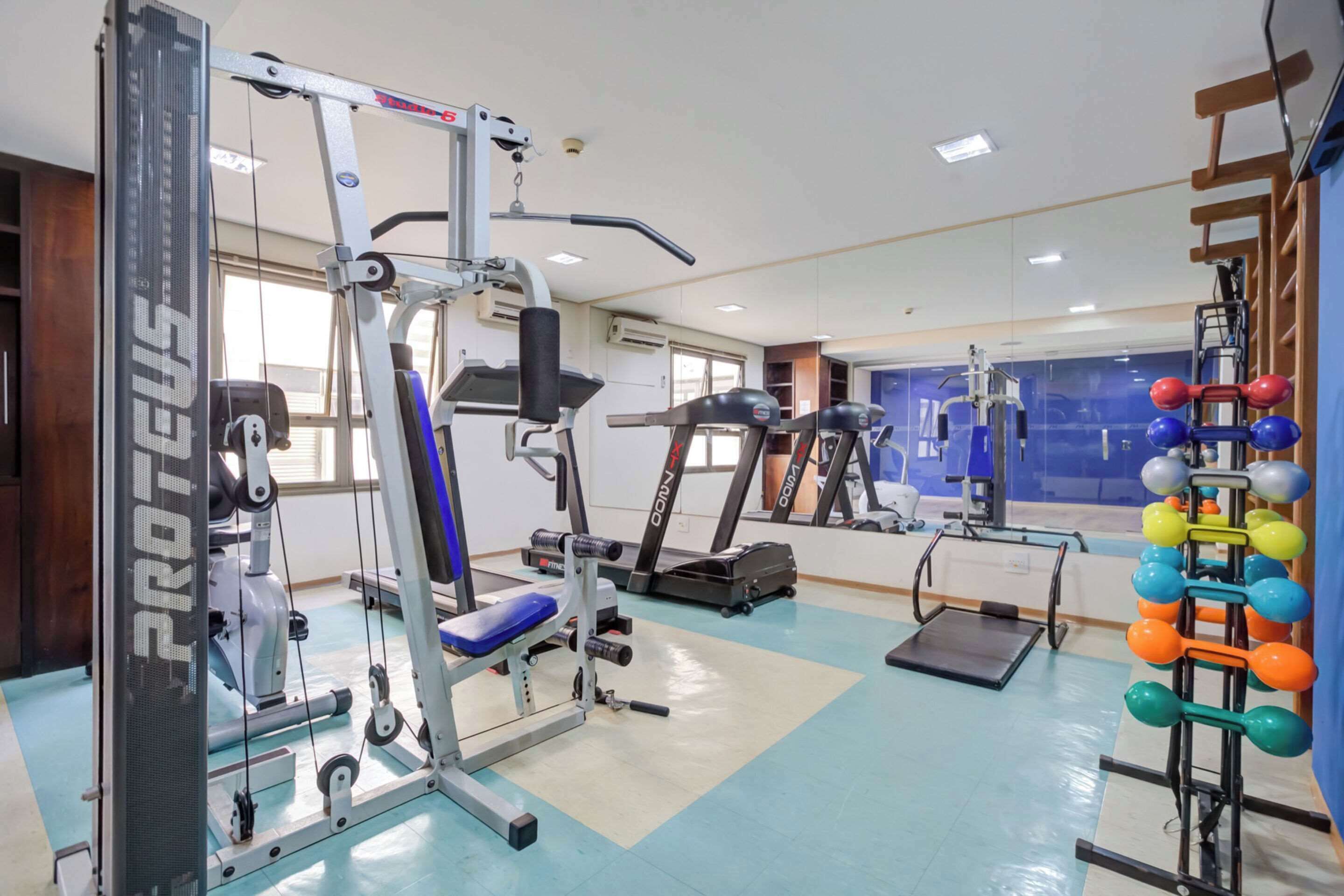 Een sportschool met cardioapparatuur, gewichten en een spiegelwand.