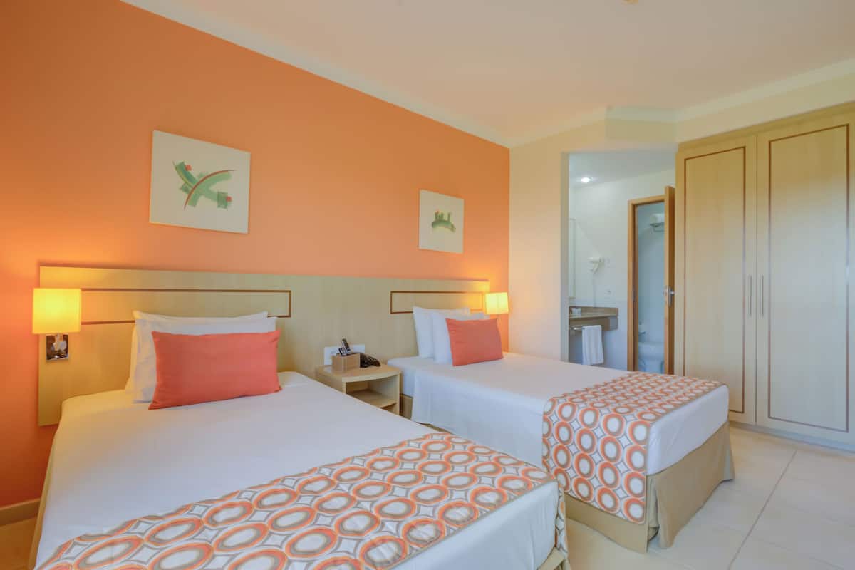 Habitación de hotel con dos camas, cada una con colcha estampada, una mesita de noche con lámpara y un cuadro colgado en la pared.