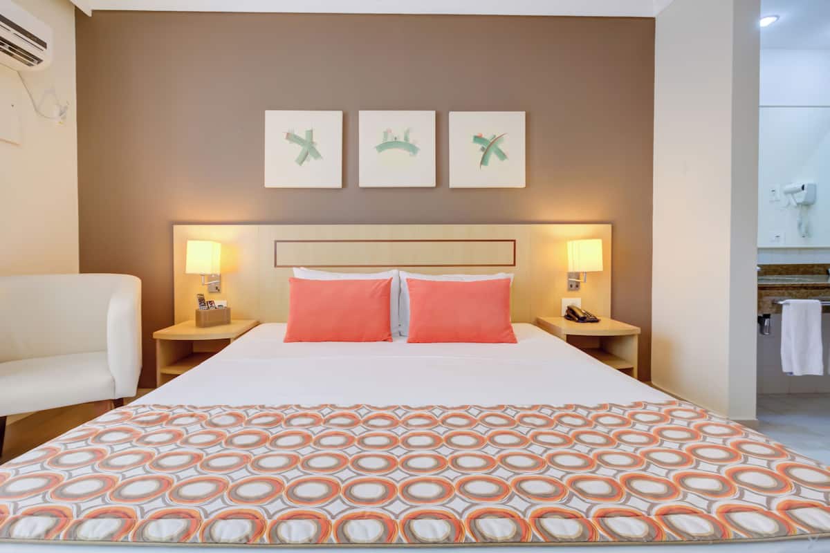 Una habitación de hotel con una cama grande, dos lámparas de noche, un sofá blanco y tres obras de arte colgadas en la pared.