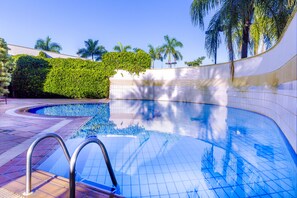 A swimming pool with a tiled edge, surrounded by a white wall and lush greenery.
