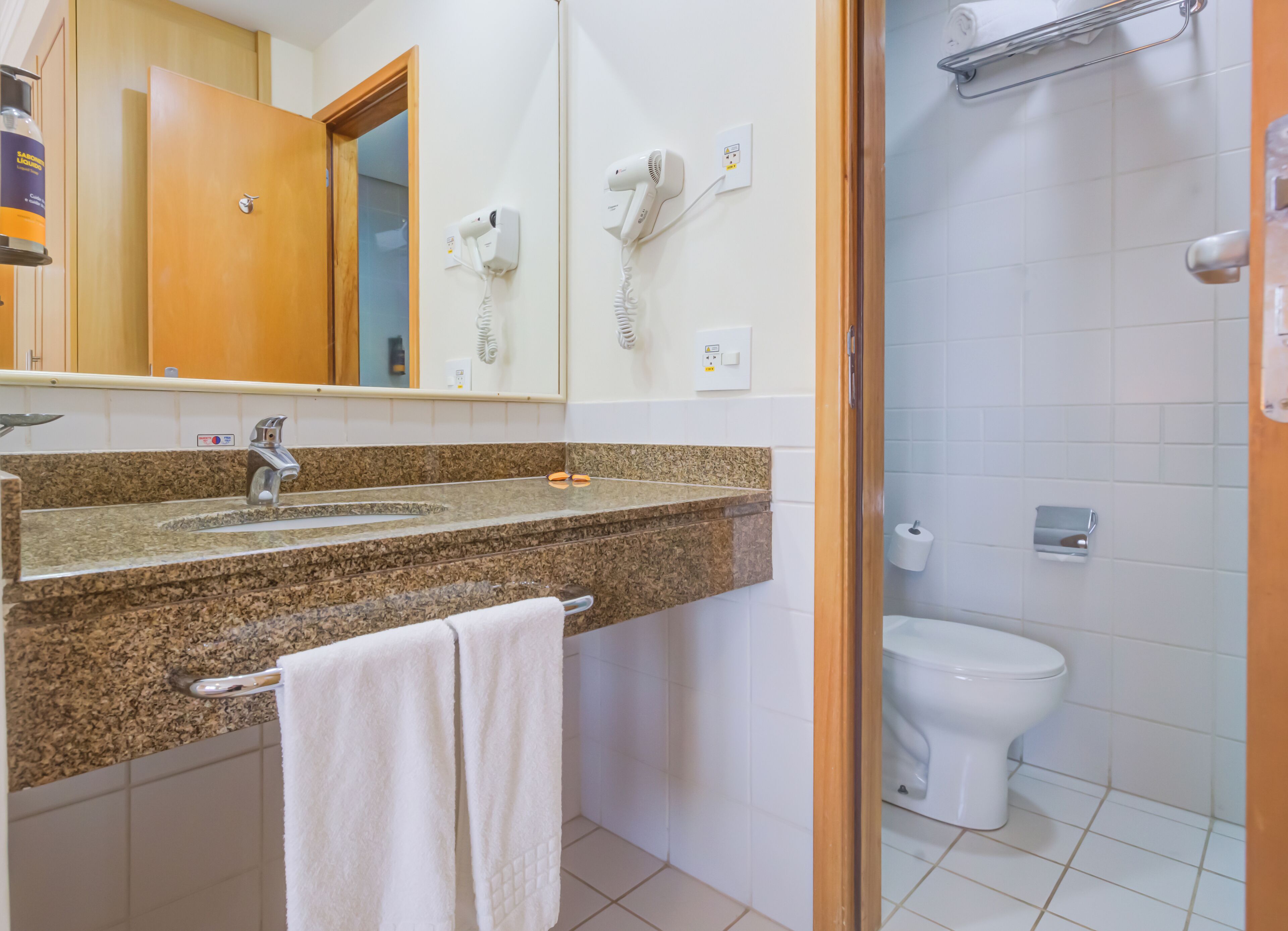 Een badkamer met een granieten aanrechtblad, een wastafel, een spiegel, een handdoekhouder, een toilet en een douchehoek.