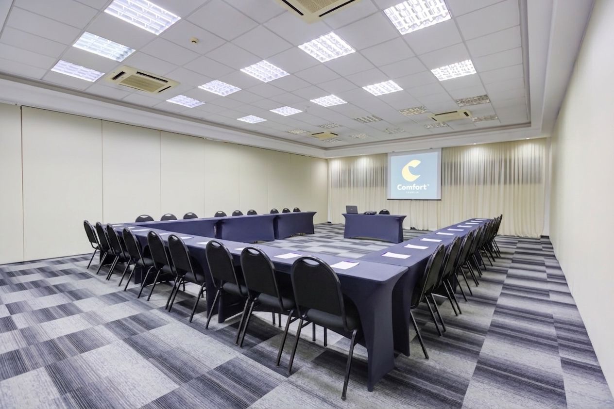 Un salón de conferencias con una larga mesa, sillas, un atril y una pantalla mostrando un logotipo.
