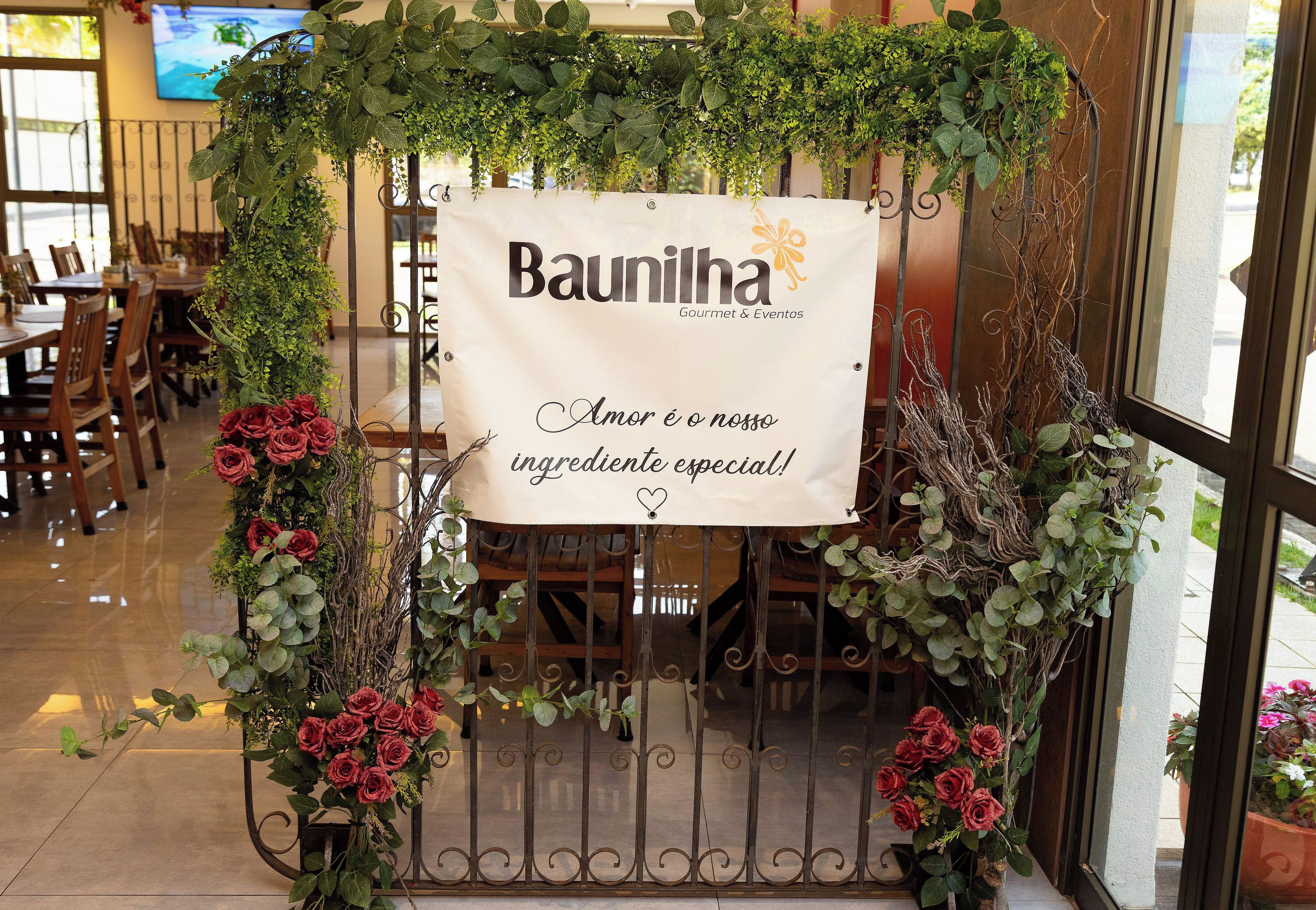 A restaurant entrance with a sign reading 'Baunilha Gourmet & Eventos' and a banner stating 'Amor é o nosso ingrediente especial!'
