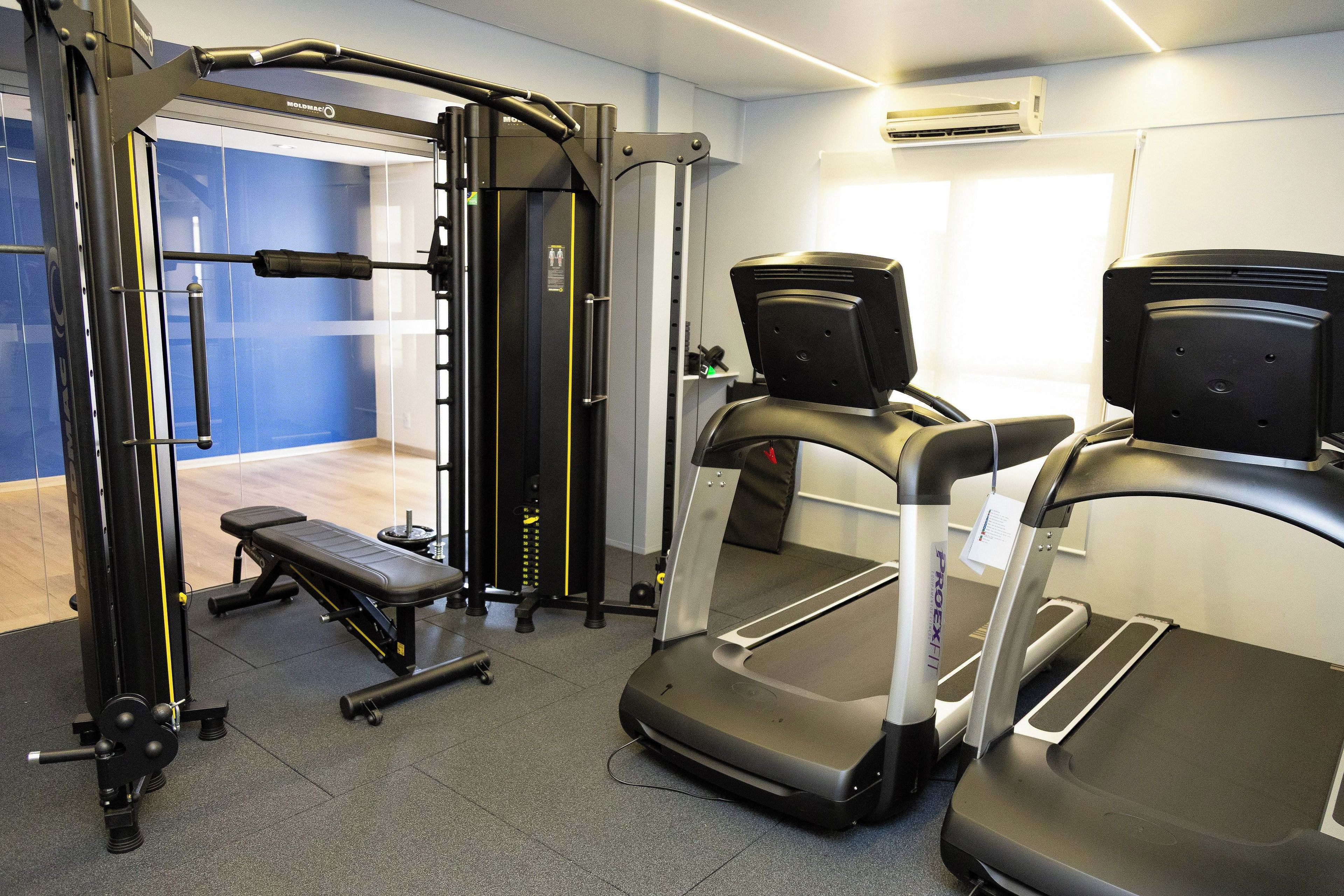 Un gimnasio con una variedad de equipos de ejercicio, incluyendo una banca, una jaula para sentadillas y una cinta de correr.