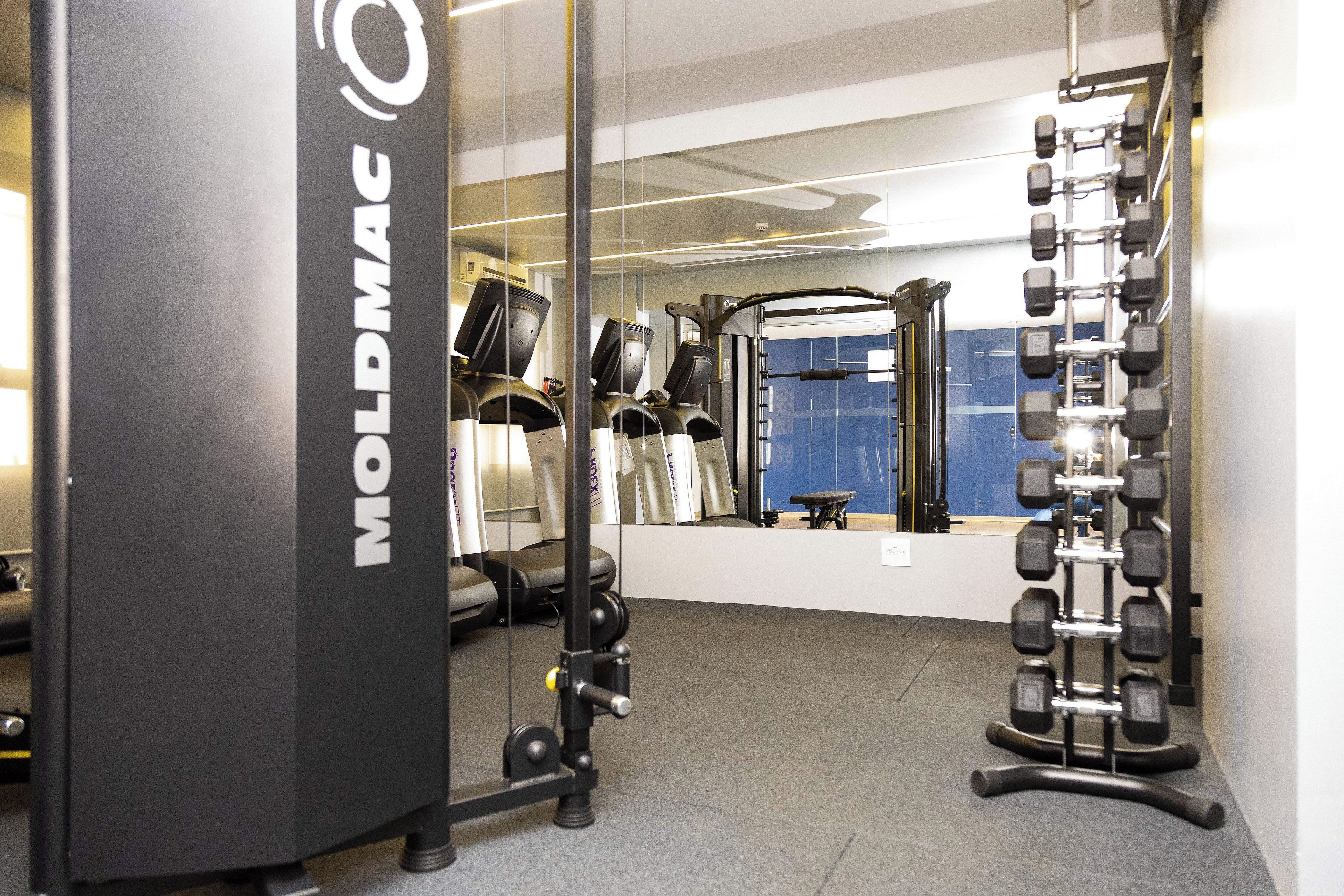 A gym with a mirrored wall, weight racks, and exercise equipment.