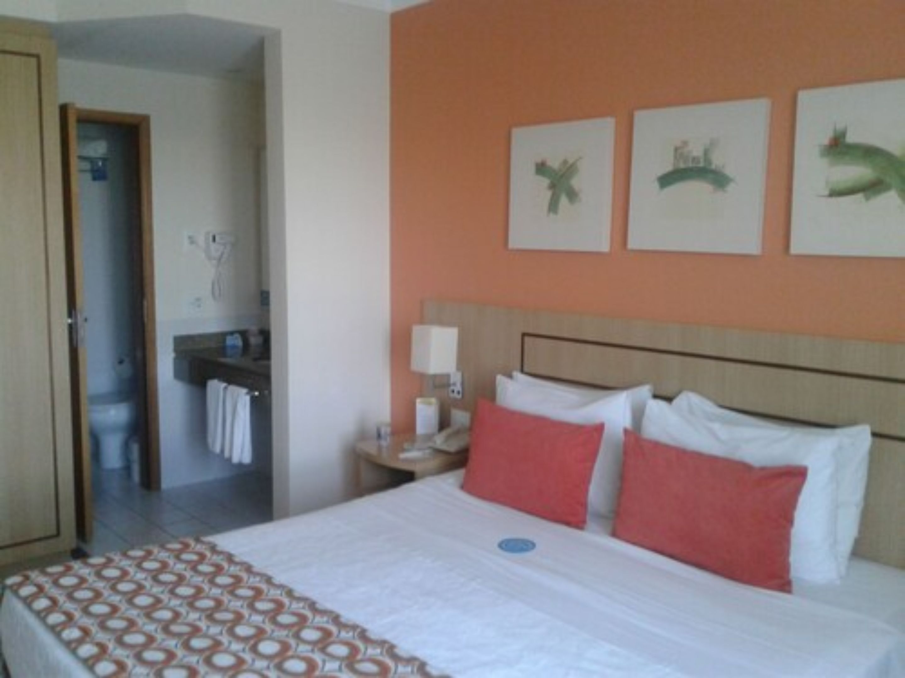 Ein Hotelzimmer mit einem Bett, einem Nachttisch und einer Wand mit drei gerahmten Bildern.