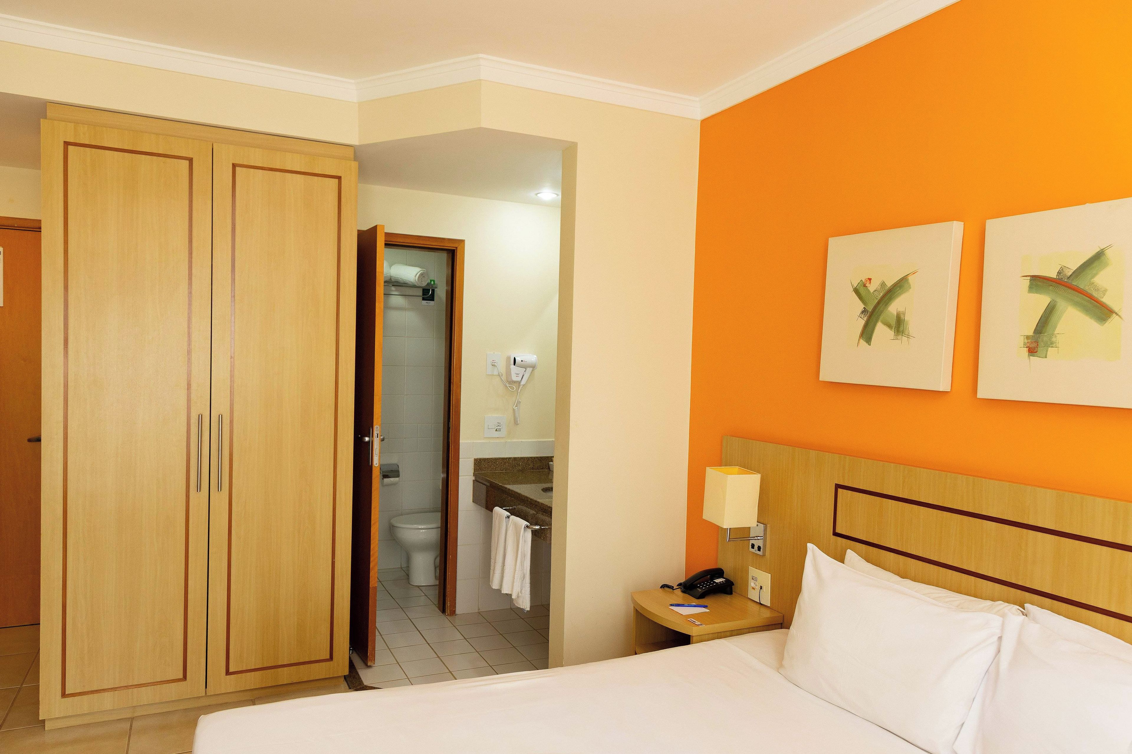 Une chambre d’hôtel avec un lit, une table de chevet, une armoire et une salle de bain visible à travers une porte ouverte.
