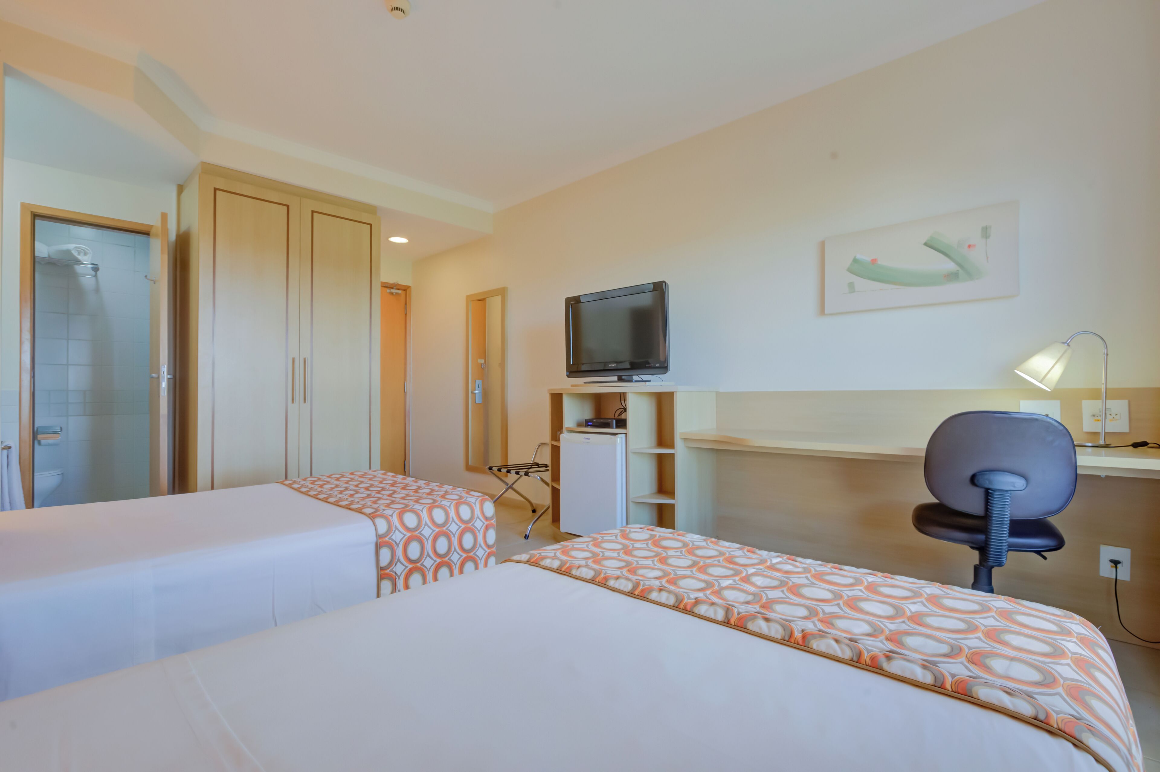 Ein Hotelzimmer mit zwei Betten, einem Schreibtisch, einem Fernseher und einer Dusche.