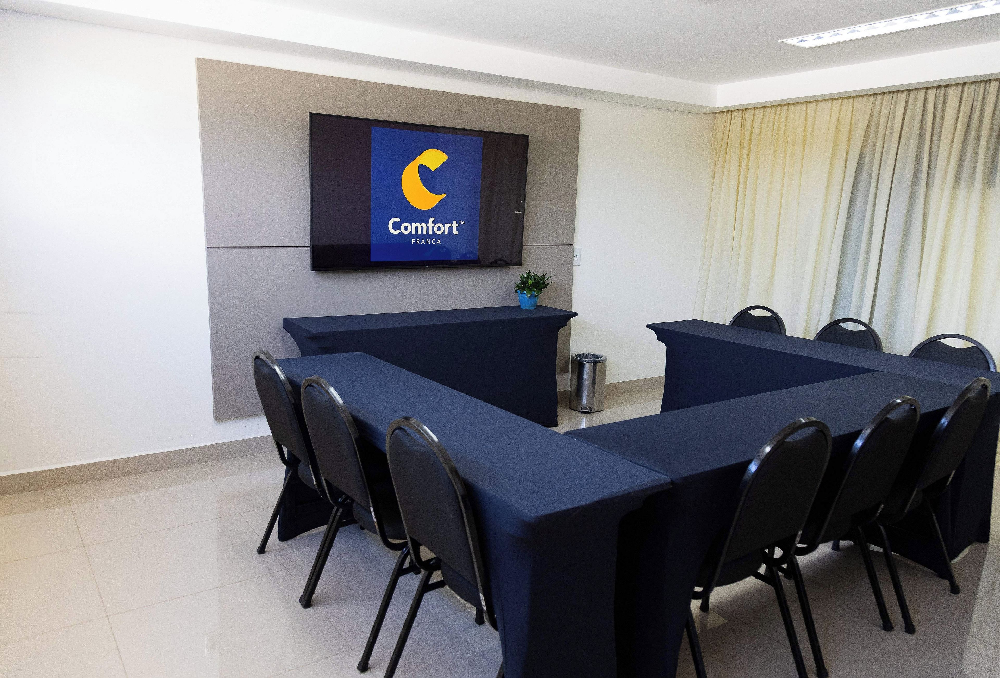 A conference room with a long table, chairs, a TV screen displaying a logo, and a potted plant.