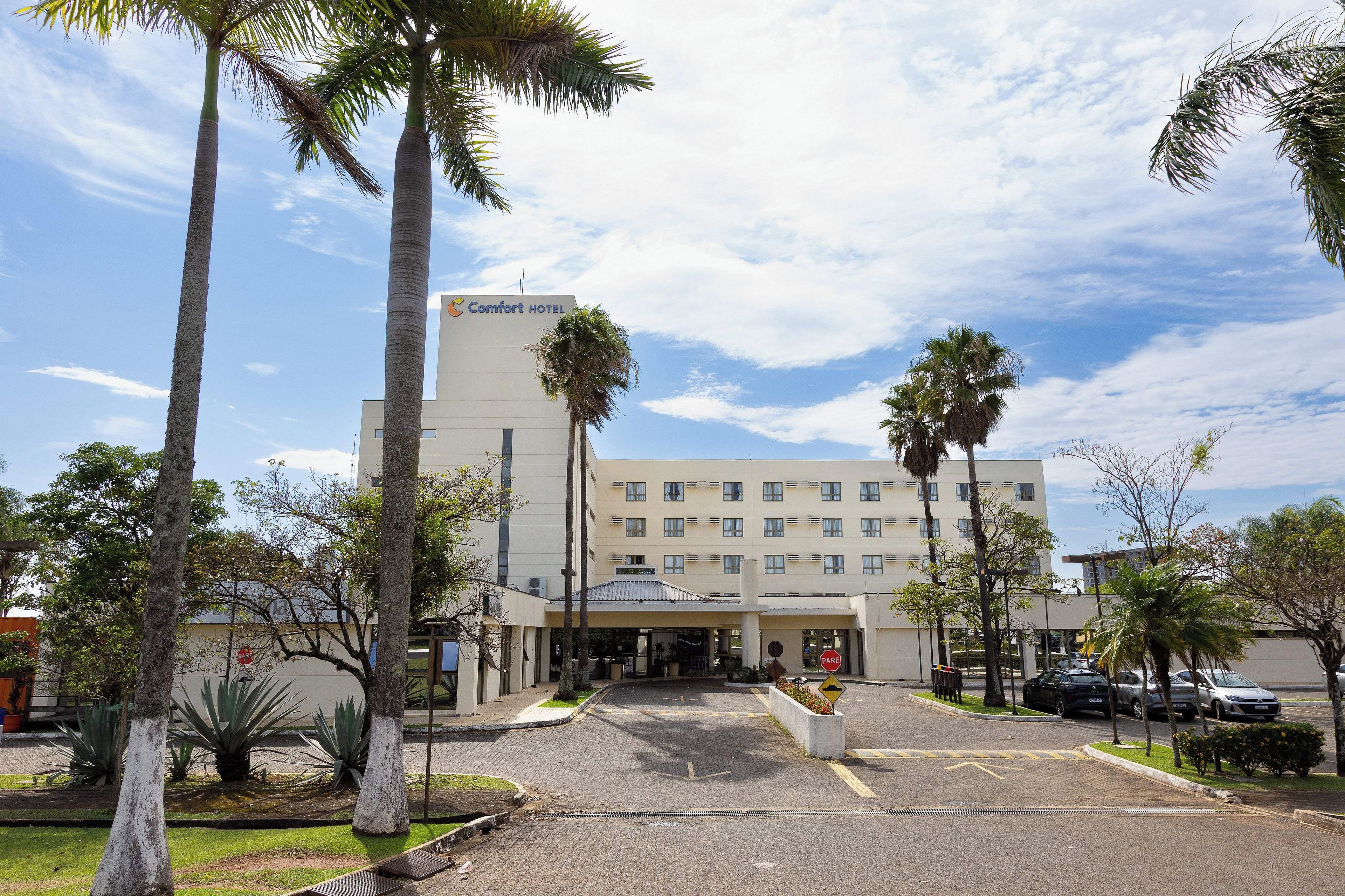 Un hotel con entrada principal, palmeras y zona de estacionamiento.