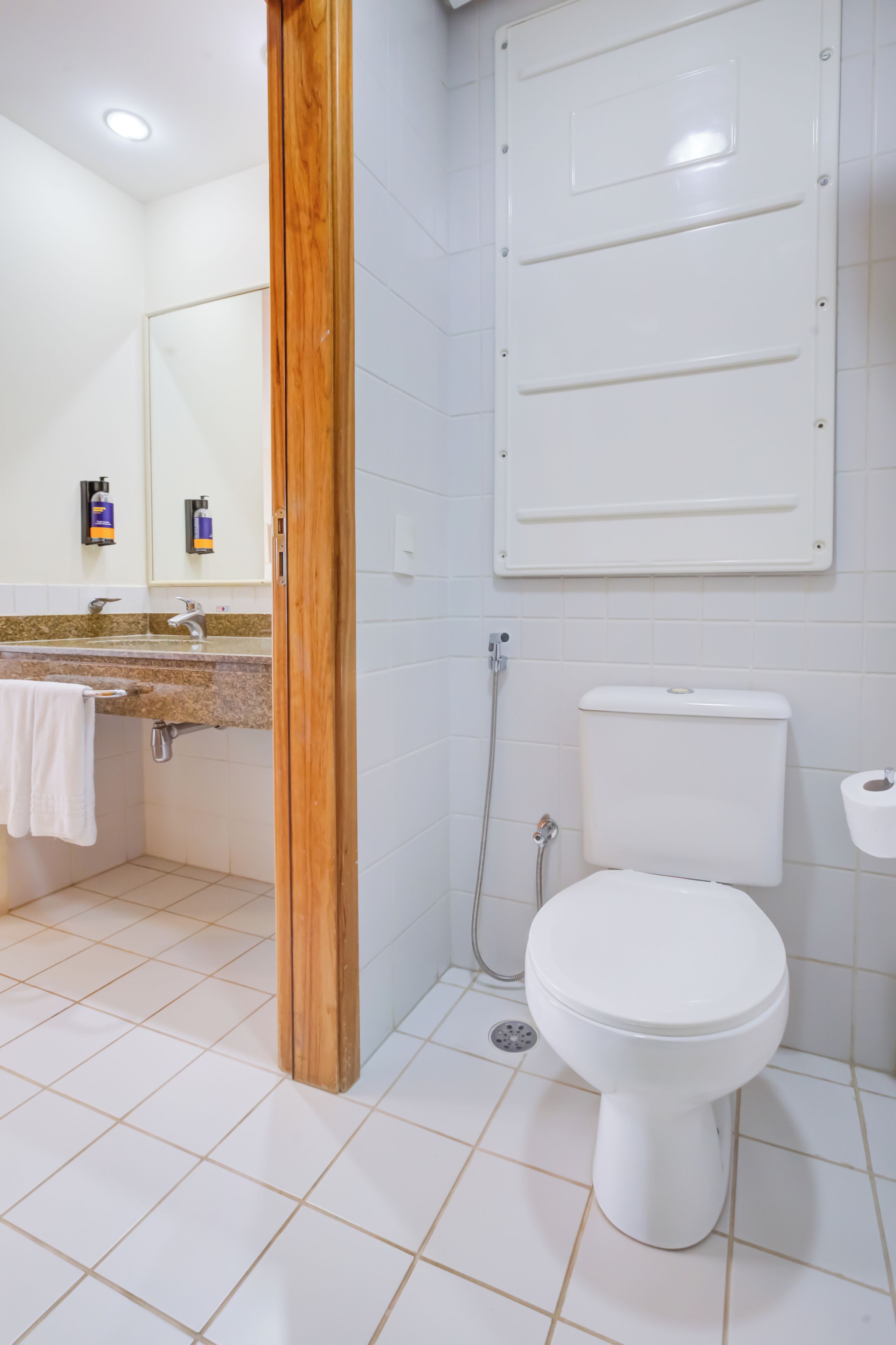 Un baño con inodoro blanco, lavamanos con toalla y ducha.