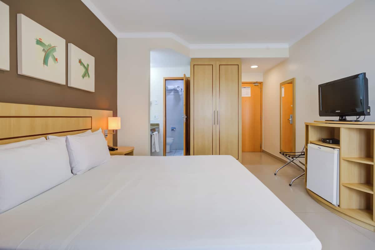 Una habitación de hotel con una cama grande, televisión, escritorio con lámpara y armario.