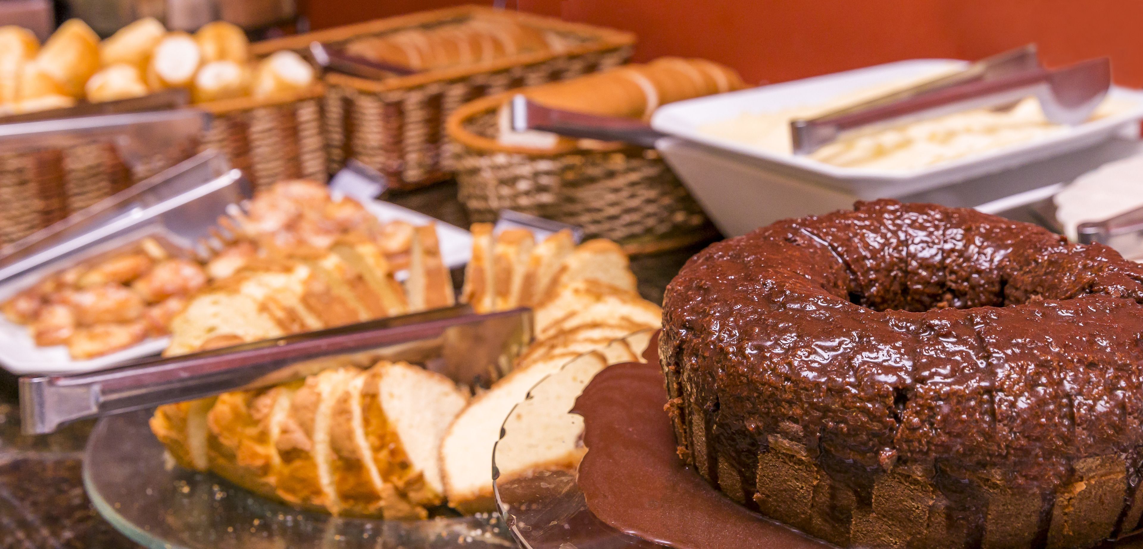 Un bufé con diversos alimentos, incluyendo un pastel de chocolate y pan en rebanadas.