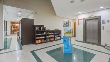 Um lobby moderno e limpo, com uma mesa de recepção, máquina de vendas automática e elevador.