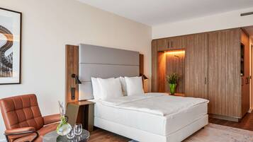 A modern bedroom with a large bed, a brown leather chair, a small round table with glasses, and a framed picture on the wall.