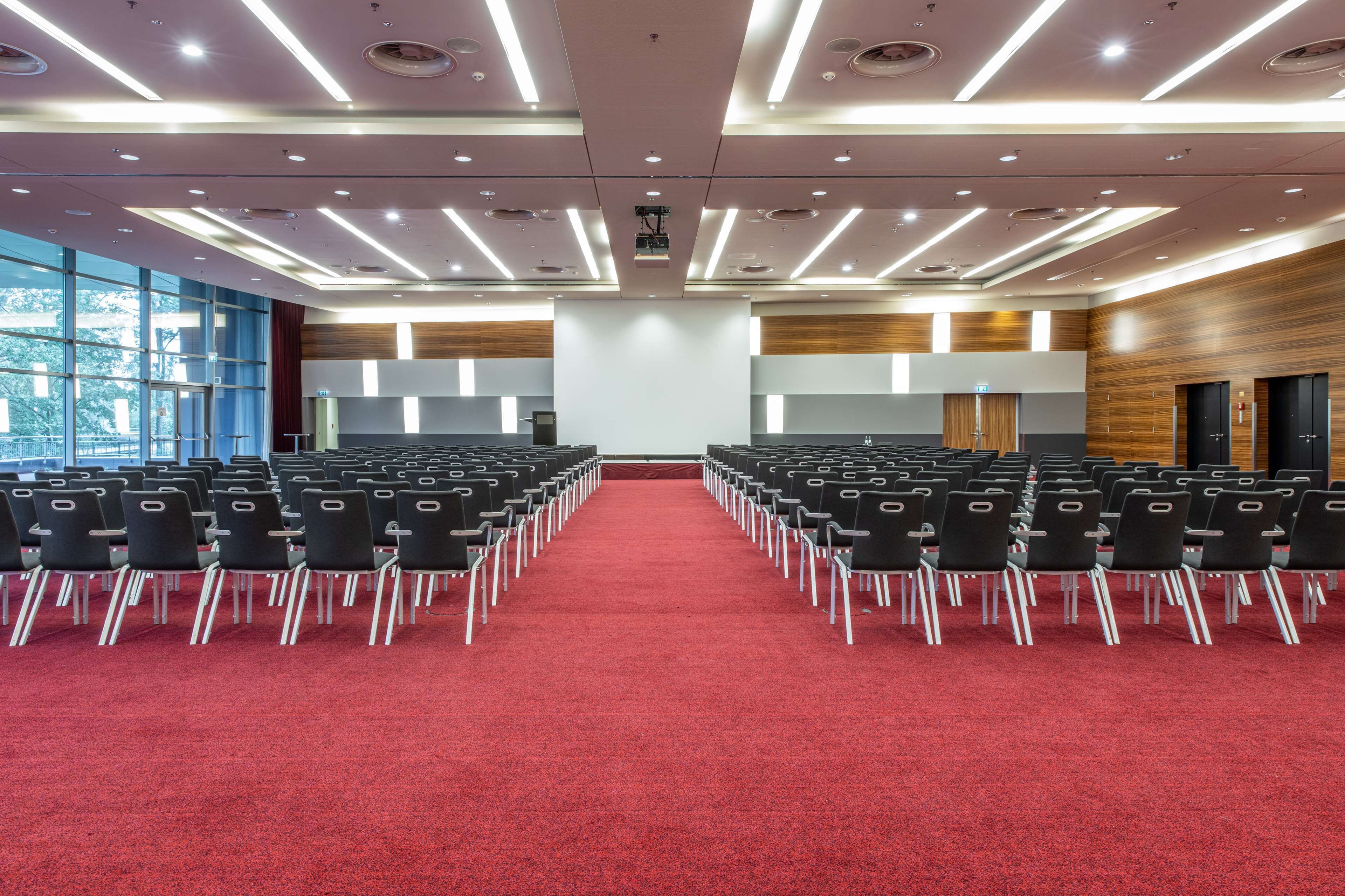 A conference room with rows of chairs, a red carpet, and a large window on the left.