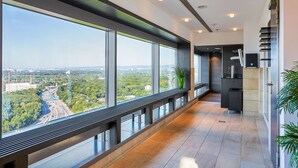 A modern hotel corridor with large windows offering a city view, a long bench, and a staircase. - Radisson Blu Hotel, Frankfurt (Frankfurt)