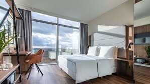 A modern hotel room with a large bed, a desk with a chair, a large window with curtains, and a view of the city. - Radisson Blu Hotel, Frankfurt (Frankfurt)
