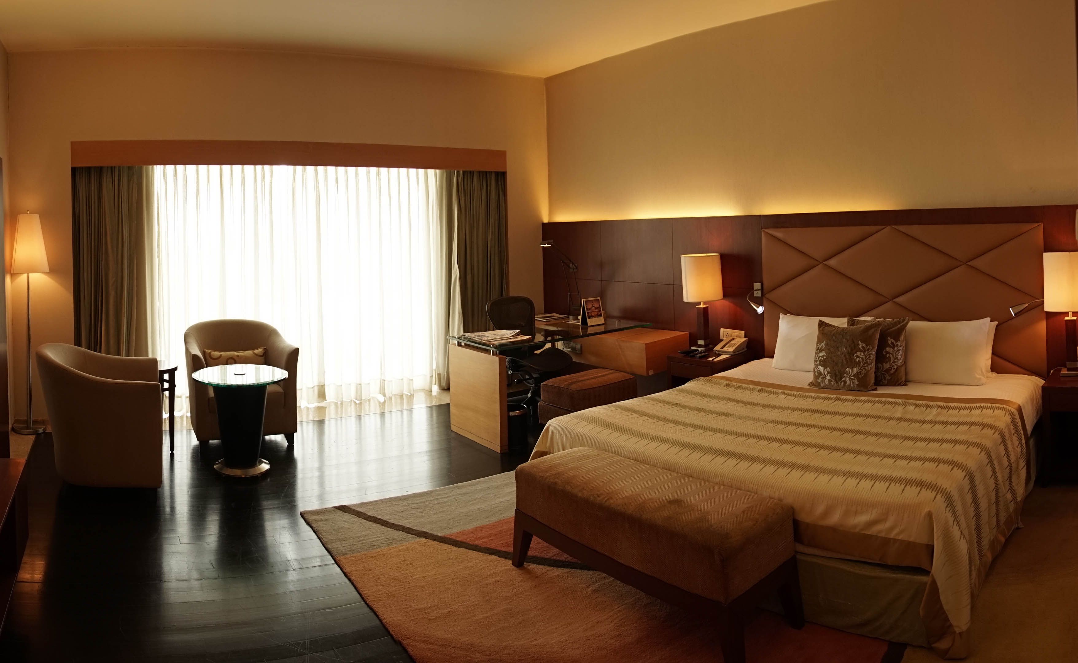 A hotel room with a large bed, a desk, a chair, and a window with curtains.