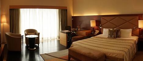 A hotel room with a large bed, a desk, a chair, and a window with curtains.