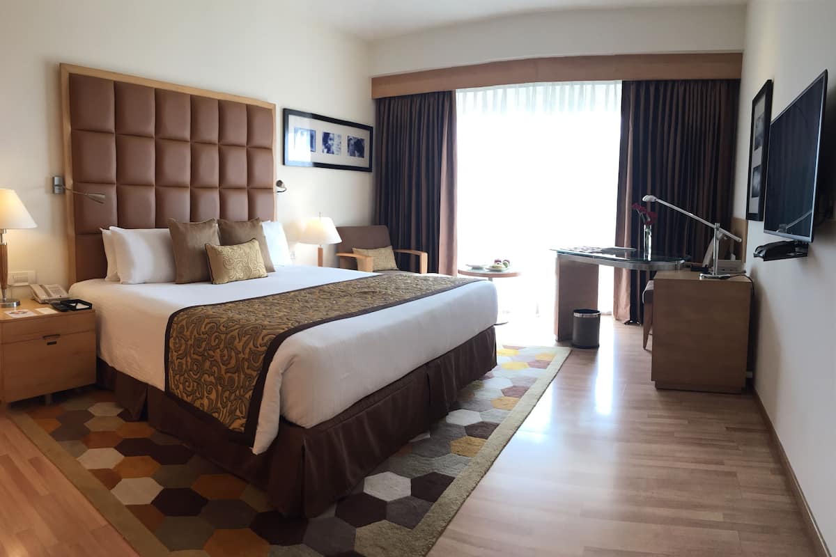 A hotel room with a large bed, a desk, a chair, a TV, and a window with curtains.