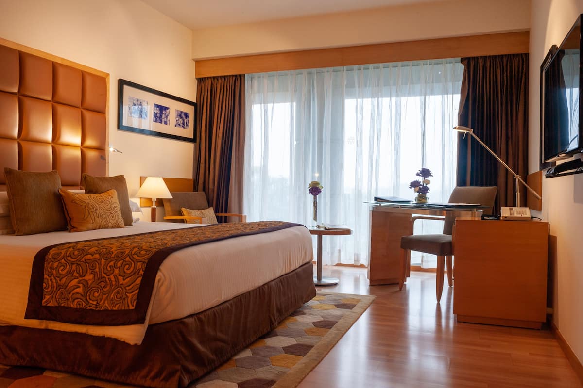 A hotel room with a large bed, a desk, a chair, a lamp, and a television.