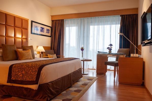 A hotel room with a large bed, a desk, a chair, a lamp, and a television. - Taj Chandigarh (Chandigarh)