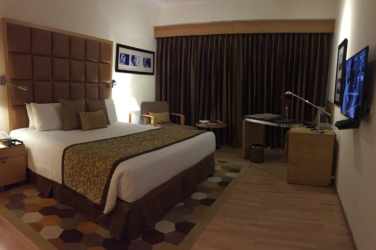 A hotel room with a large bed, a desk, a television, and a chair.