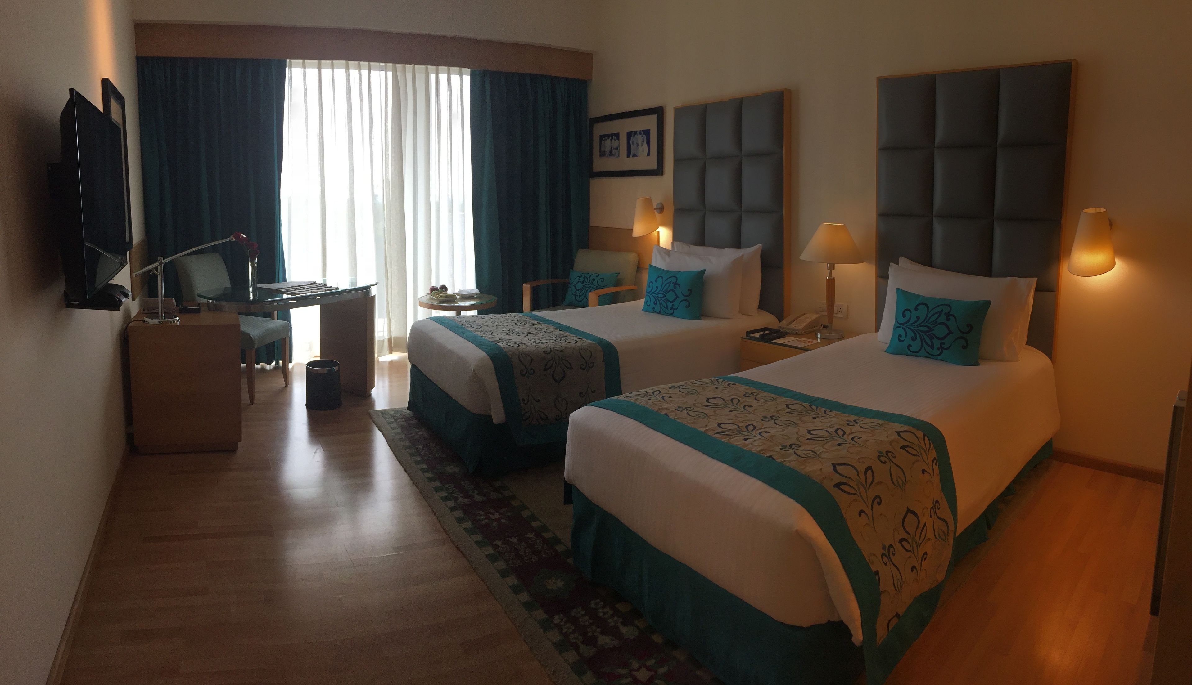 A hotel room with two beds, a desk, a TV, and a window with curtains.