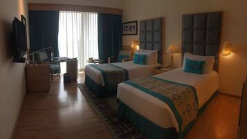 A hotel room with two beds, a desk, a TV, and a window with curtains.