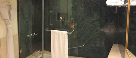 A glass-enclosed shower with a white towel, a glass-enclosed bathtub, and a glass-enclosed vanity with a towel rack.
