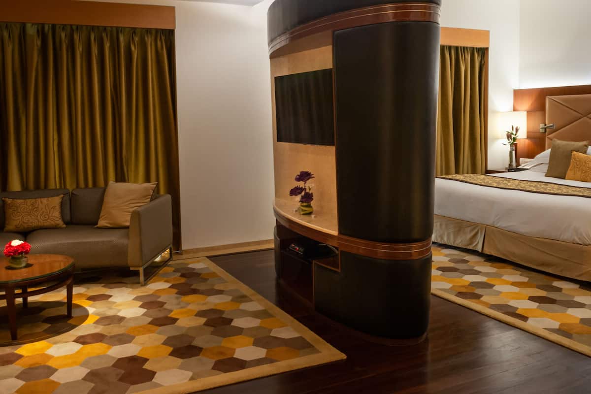 A hotel room with a sofa, a bed, a curved partition, and a patterned rug.