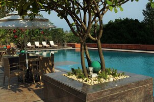 Zona de piscina con sillones de descanso, una mesa con sillas y un macetero decorativo.