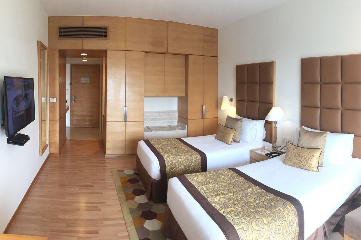 A hotel room with two beds, a sofa, a TV, a desk, and a wardrobe.