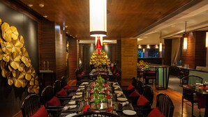 Un restaurant doté d’une longue table à manger, de chaises noires avec des coussins rouges, et d’un mur décoratif orné de motifs dorés.