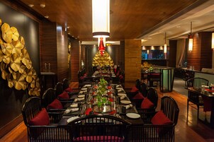 Un restaurante con una larga mesa de comedor, sillas negras con cojines rojos y una pared decorativa con motivos de hojas doradas.