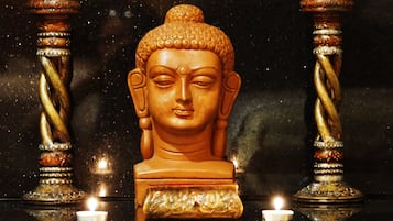 Una estatua de Buda con intrincados grabados, ubicada entre dos columnas retorcidas, con una vela encendida en primer plano.