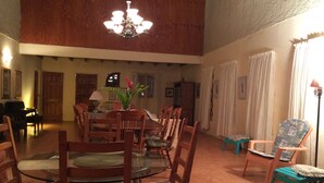 A dining area with a round glass table surrounded by wooden chairs, a chandelier, and a piano in the background. - Teresinajamaica (St. Ann's Bay)