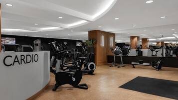 Un gimnasio moderno con equipo de cardio, un mostrador de recepción que dice 'CARDIO' y un espejo grande que refleja el espacio.