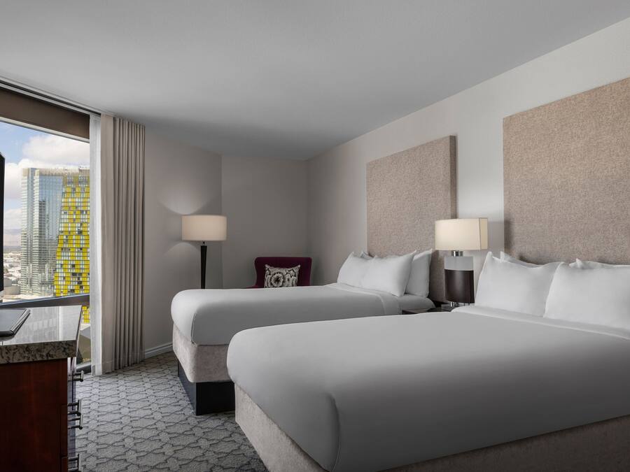 Una camera d'albergo con due letti, una scrivania e vista sulla città.